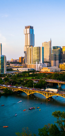 Aerial view of downtown Austin skyline at sunset with high-rise buildings along the Colorado River and a boat on the water.