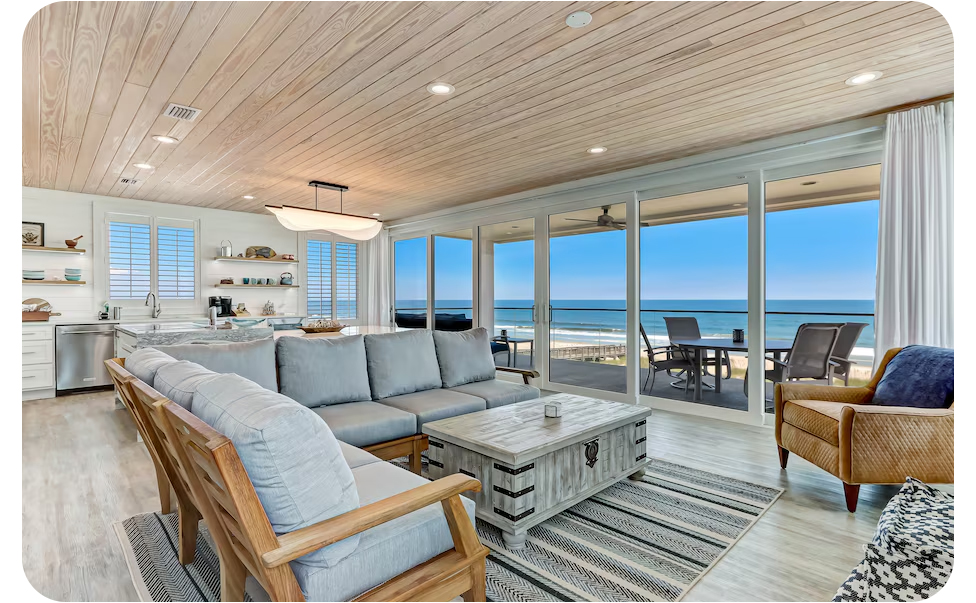 Open living area with seating and a kitchen, extending to a balcony with outdoor chairs and ocean views.