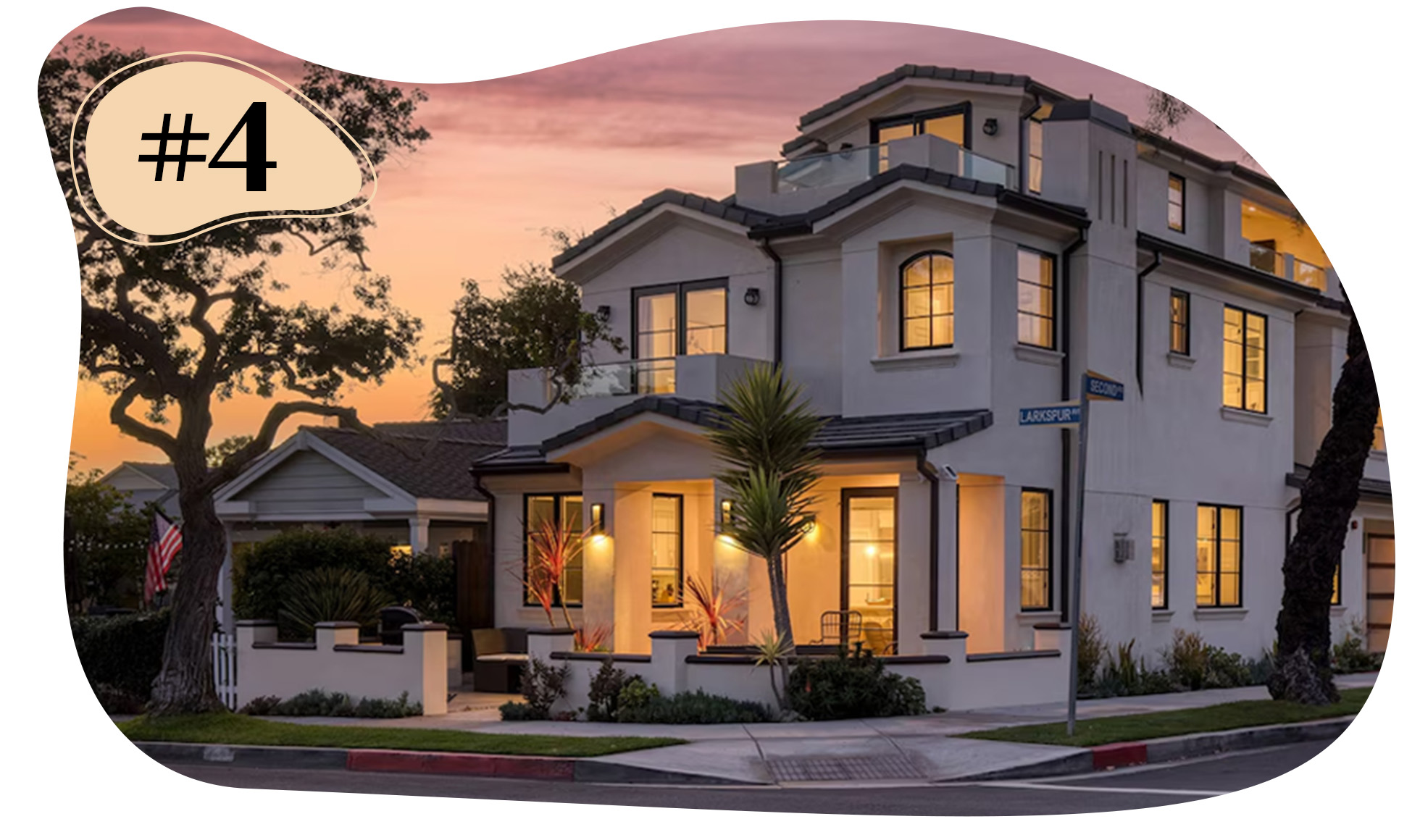 Two-story corner house at sunset with balconies, large windows, and exterior lights on.
