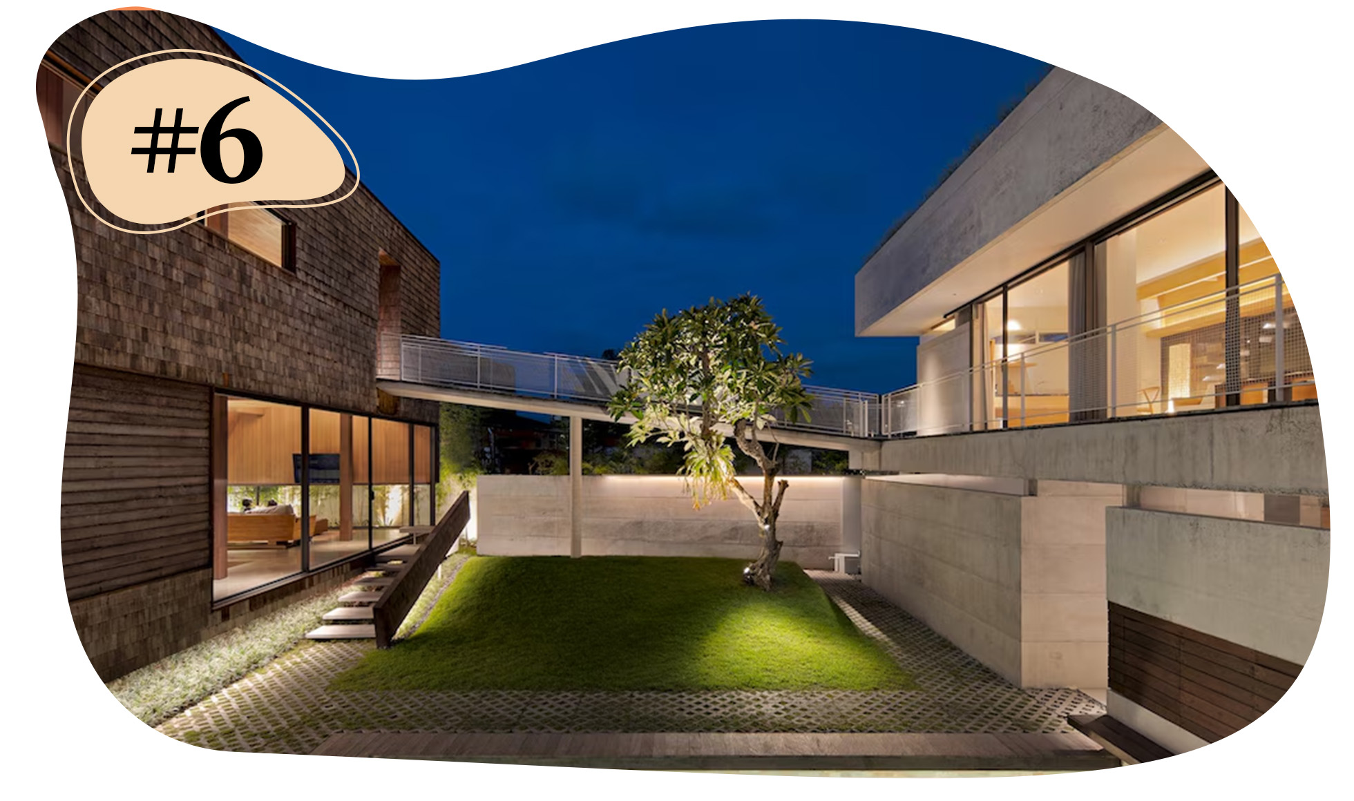 Courtyard between two buildings at night, featuring a lit tree, walkways, and interior lights.