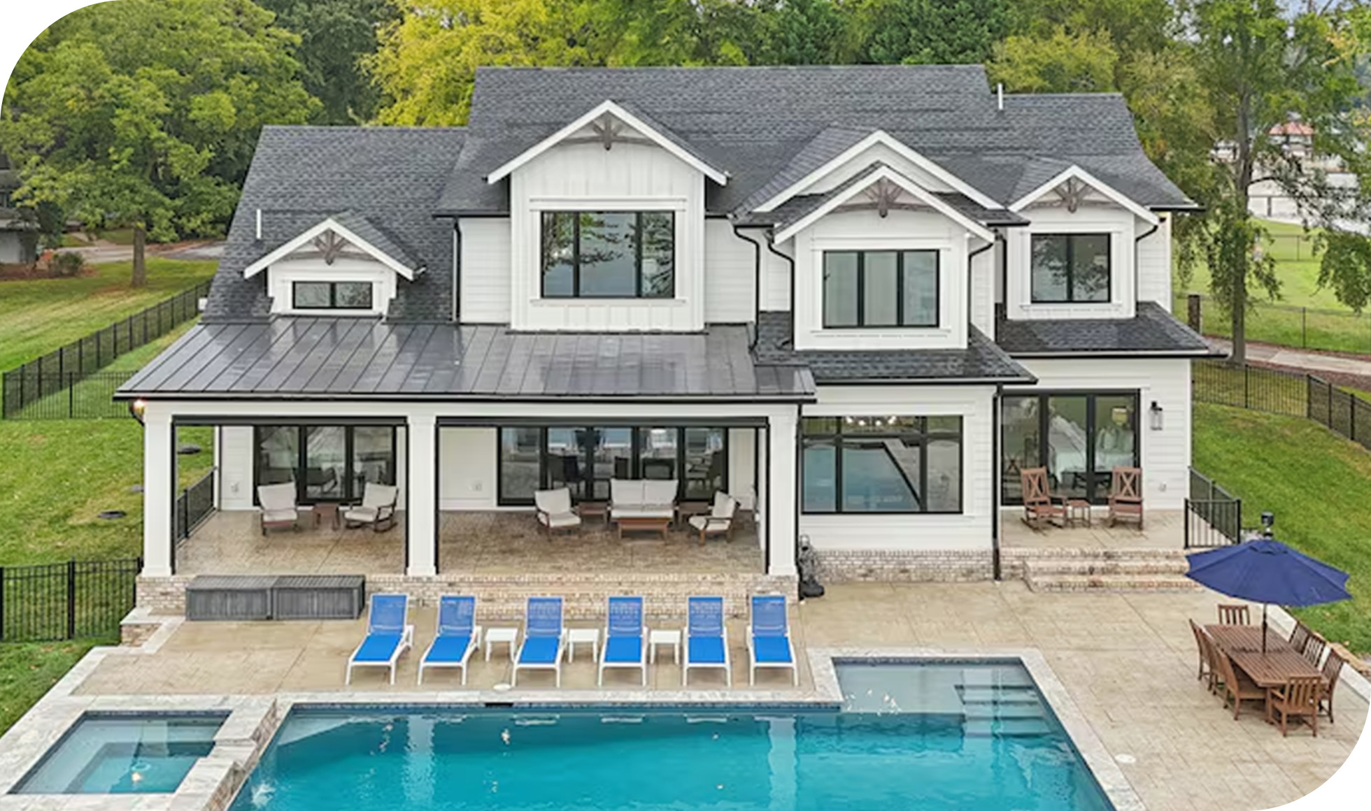 Large white-grey lakeside home with covered patio, pool, and outdoor seating.