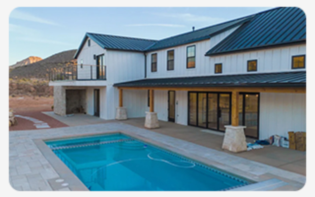 Modern desert home with metal roof, stone columns, sliding doors, and a rectangular pool.
