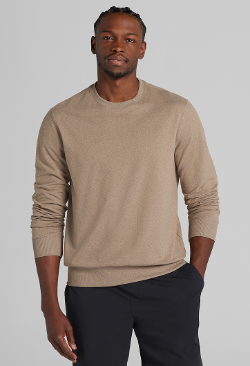 Man wearing a tan crewneck sweater with dark pants, standing against a light background.