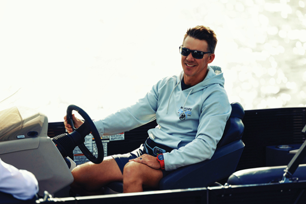 A man wearing a Mercury hoodie driving a boat