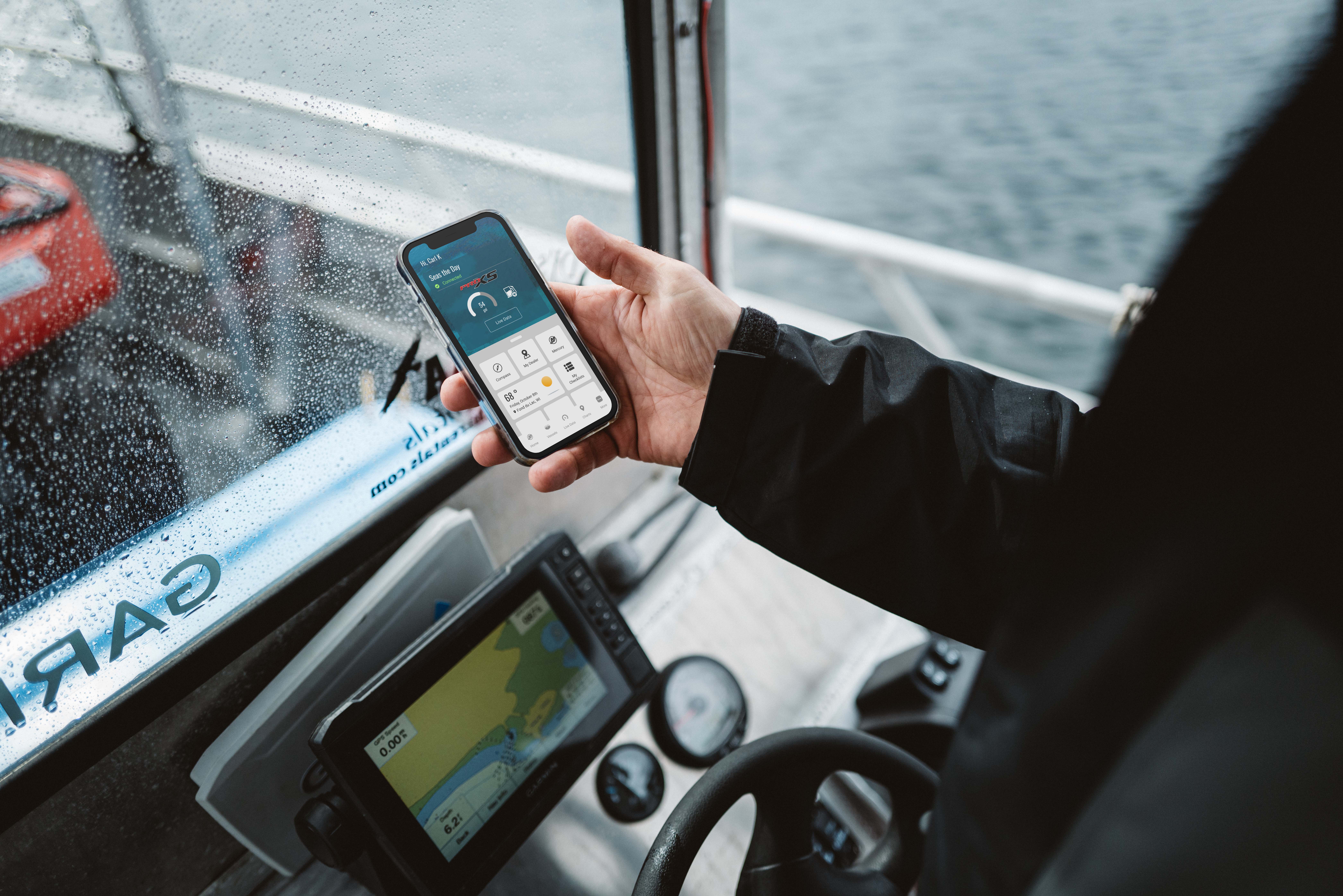 A hand holding a smartphone displaying engine data on a boat.