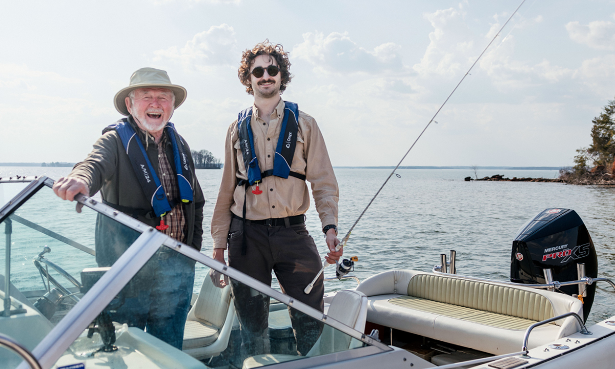 Two men smile for the camera from a motorboat on a lake.