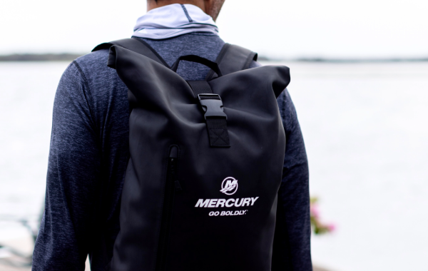 A person wearing a black Mercury backpack stands near the water.