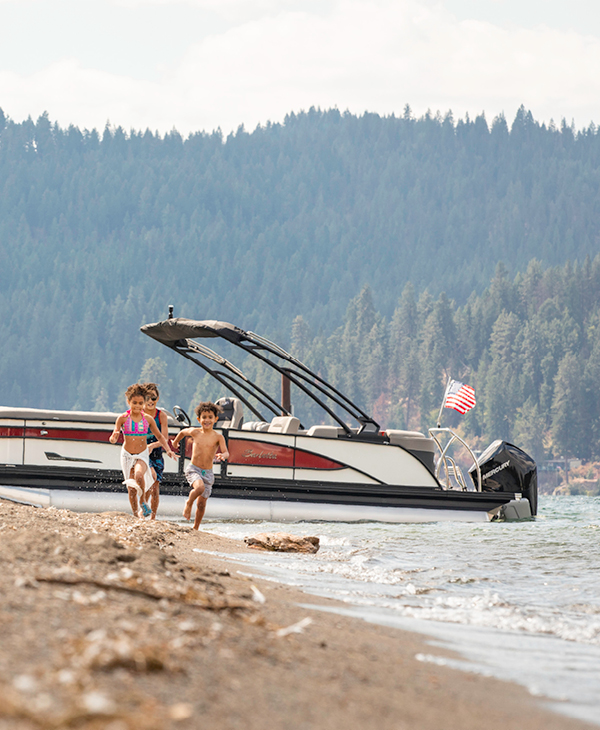 Kids enjoying a day at the lake, running near a boat on the beach.