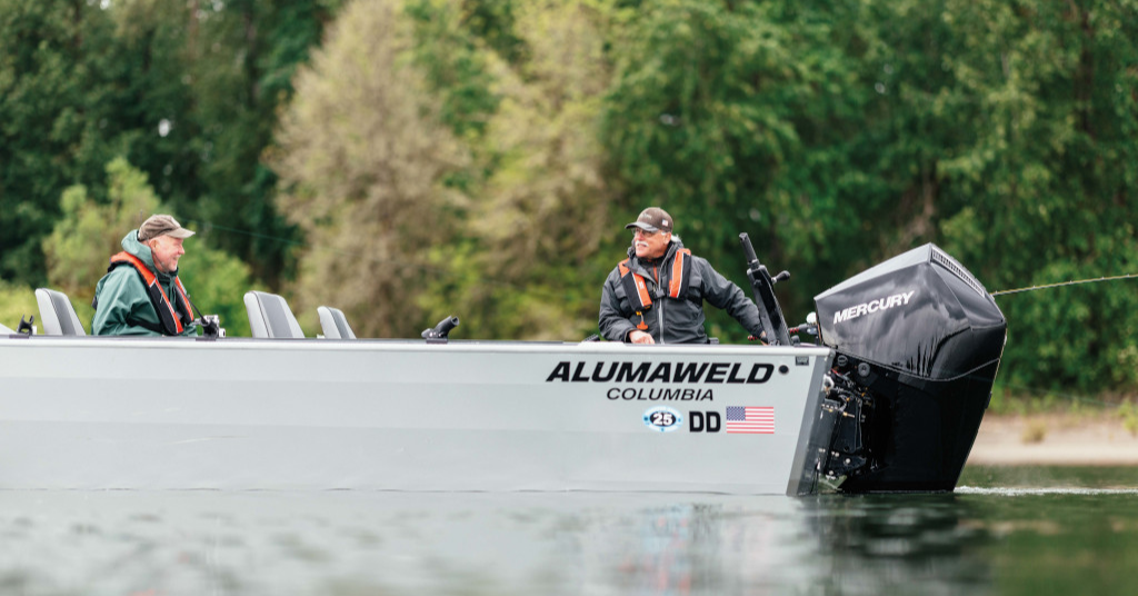 A silver Alumaweld Columbia boat with two men wearing life jackets, powered by a black Mercury outboard motor, on the water.