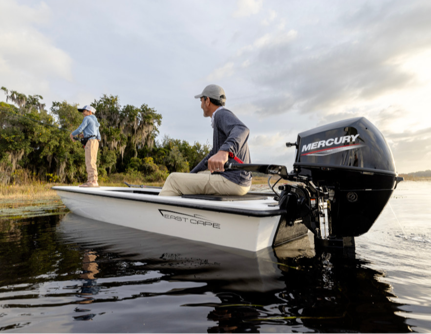 A man fishing from the front of an "East Cape" boat while another man steers from the back, featuring a "Mercury" outboard engine, on a sunny day.