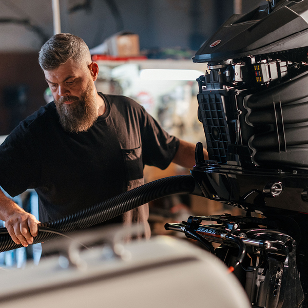 A bearded man working on a boat engine with a large hose.