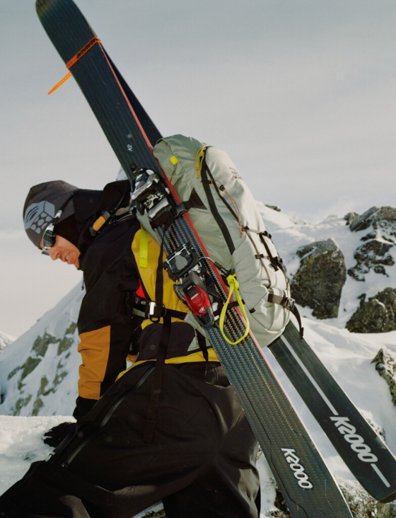 A skier carrying his skis wearing the Men's Mythogen™ Gore-Tex Pro Kit