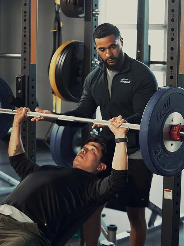 An NASM trainer helping a client with the bench press