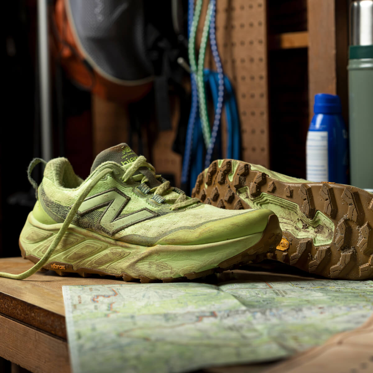 A pair of muddy, pale green New Balance sneakers sitting on a bench with a map.