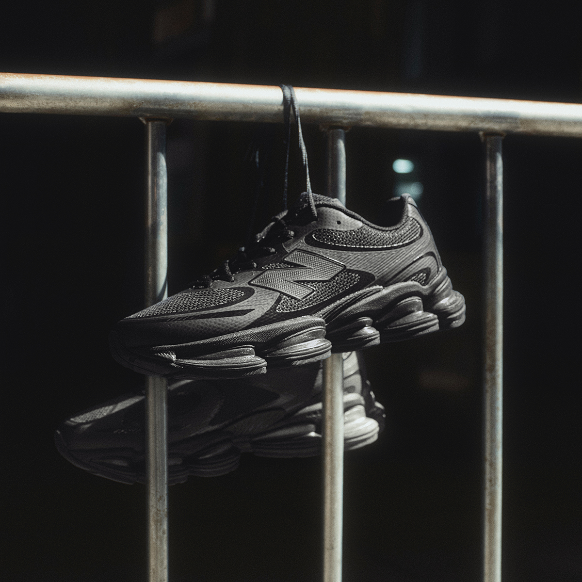 Dark New Balance shoes hanging by their shoelaces from a metal railing.