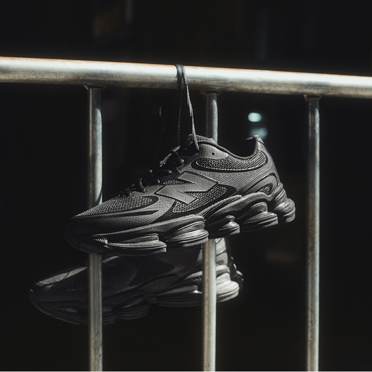 Dark New Balance shoes hanging by their shoelaces from a metal railing.