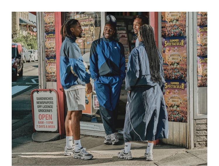 A group of four friends standing outside a bodega. All four are decked out in blue, black and grey New Balance athletic gear
