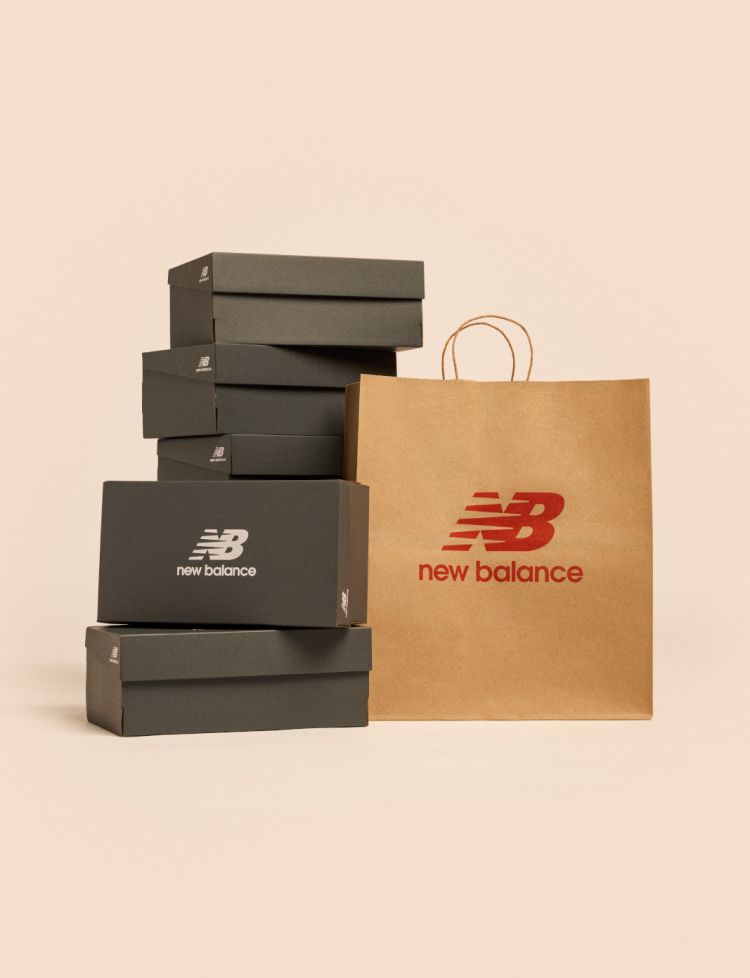 A stack of New Balance shoe boxes next to a shopping bag against a pale apricot backdrop