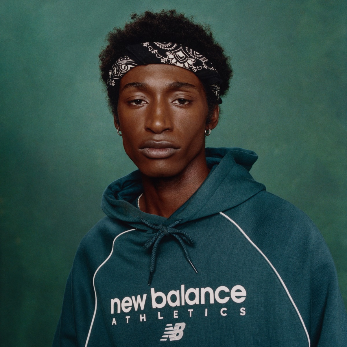 Person in a green New Balance hoodie with a Black bandana on their head.