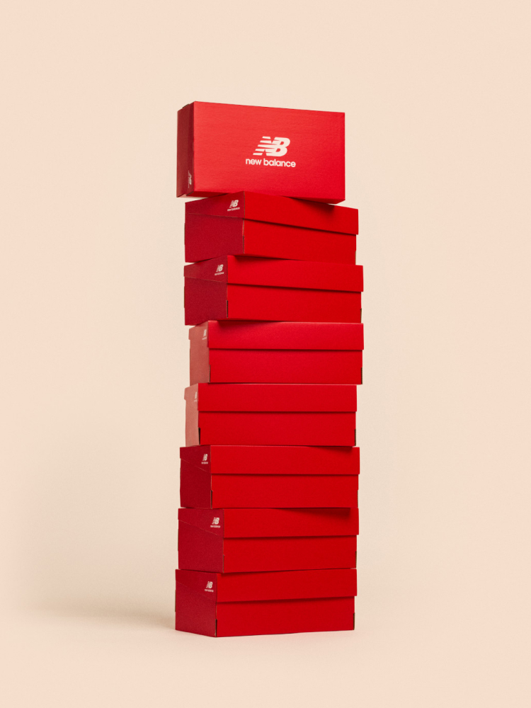 A stack of New Balance shoe boxes next to a shopping bag against a pale apricot backdrop