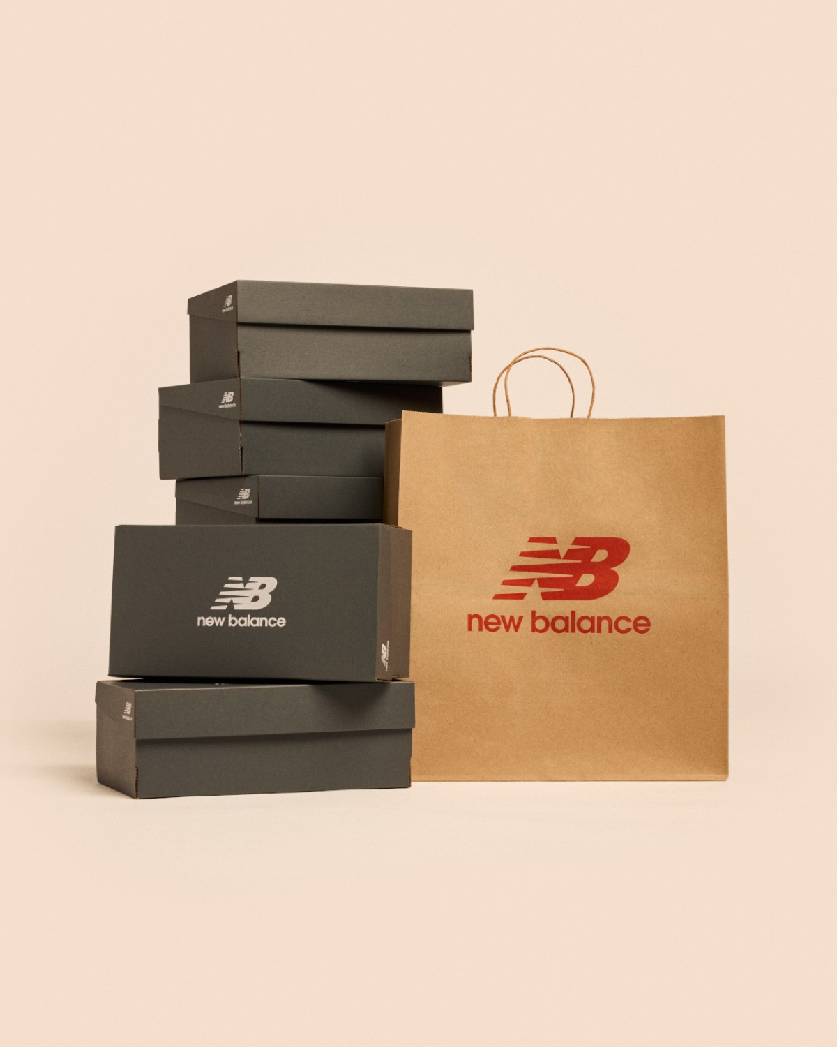 A stack of New Balance shoe boxes next to a shopping bag against a pale apricot backdrop