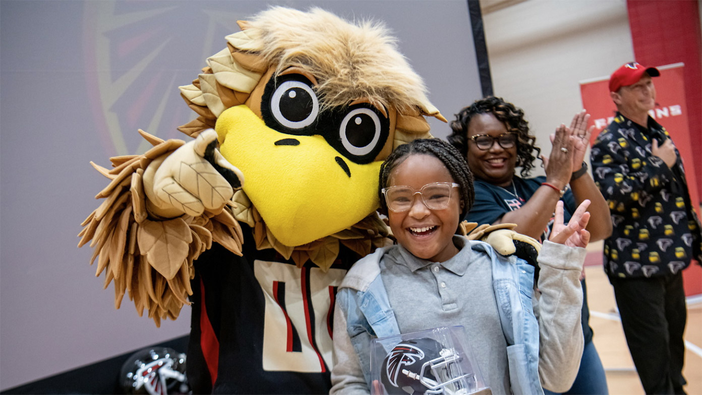 Freddie Falcon joins students at a school event, standing together in a gym