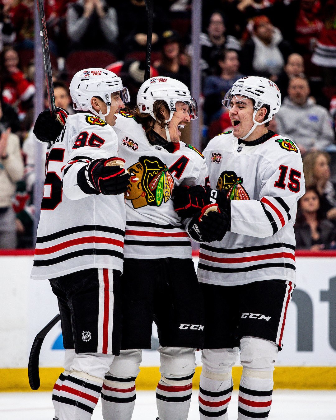 Three hockey players celebrate on the ice, smiling and embracing.