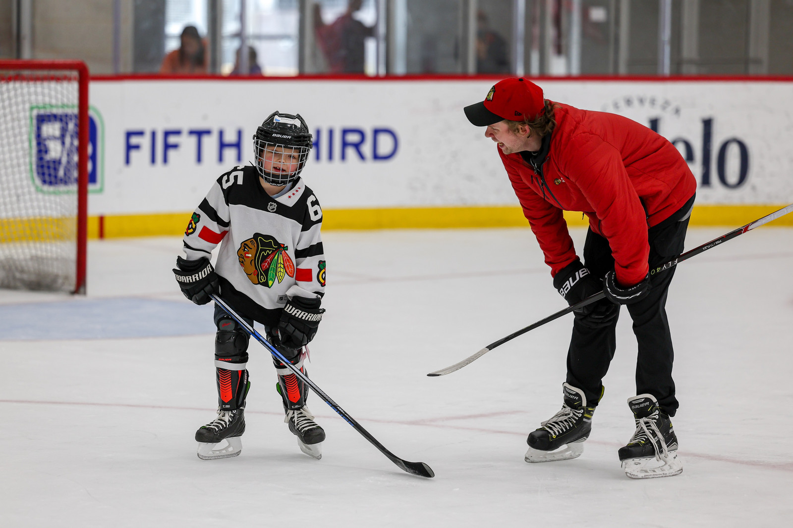 Young hockey player and coach on ice near goal.