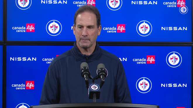 image of scott arniel being interviewed at a podium in front of an electric screen displaying various logos