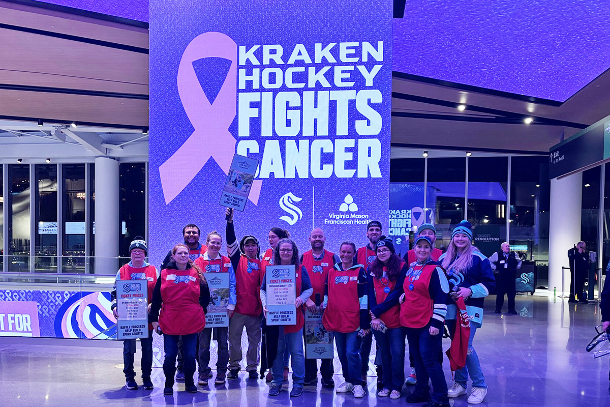 50/50 Volunteers standing in front of Kraken Hockey Fights Cancer sign