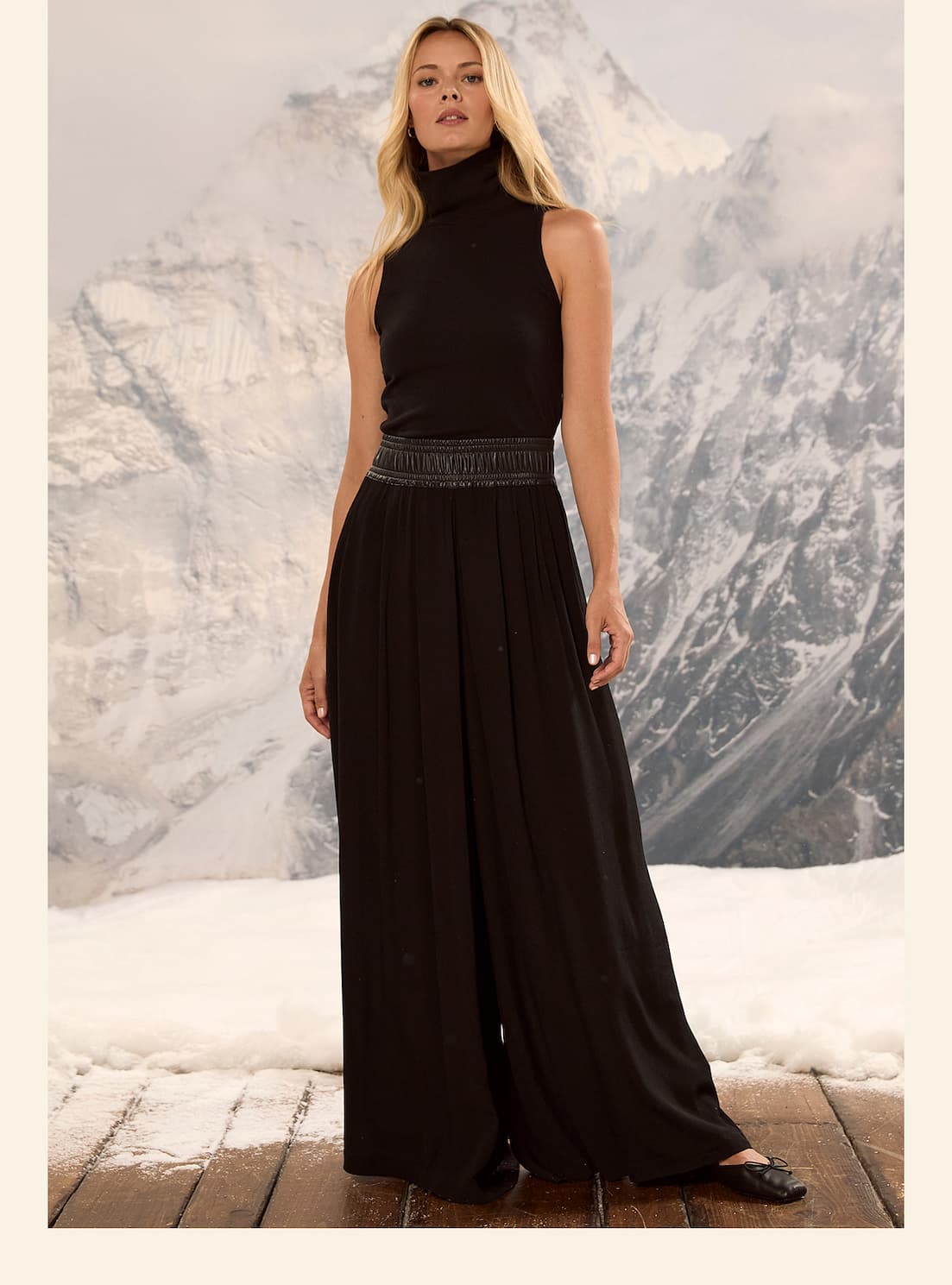 Woman wearing black pants and a black tank top against a snowy mountain background