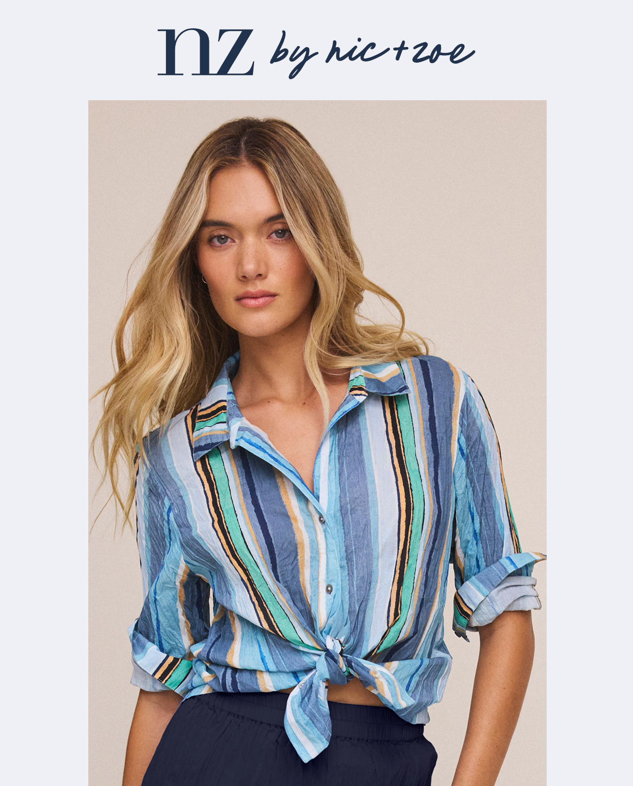 A model wearing a nz by NIC+ZOE Stripe Core Cotton Crinkle Shirt button-up shirt tied at the waist from the nz by NIC+ZOE collection.