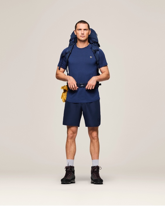 Studio shot of a man wearing a navy blue athletic shirt, shorts, and hiking boots.