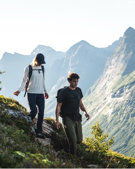 Two hikers walking down a steep, grassy mountain trail.