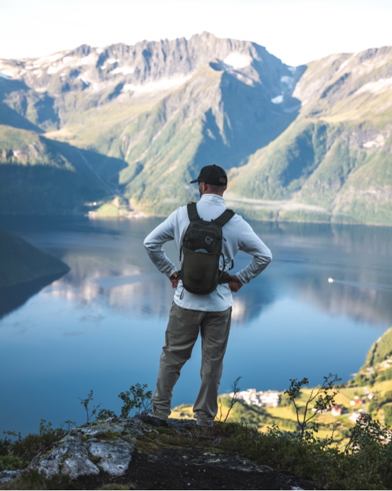 Rear view of a hiker overlooking a vast fjord and mountains.