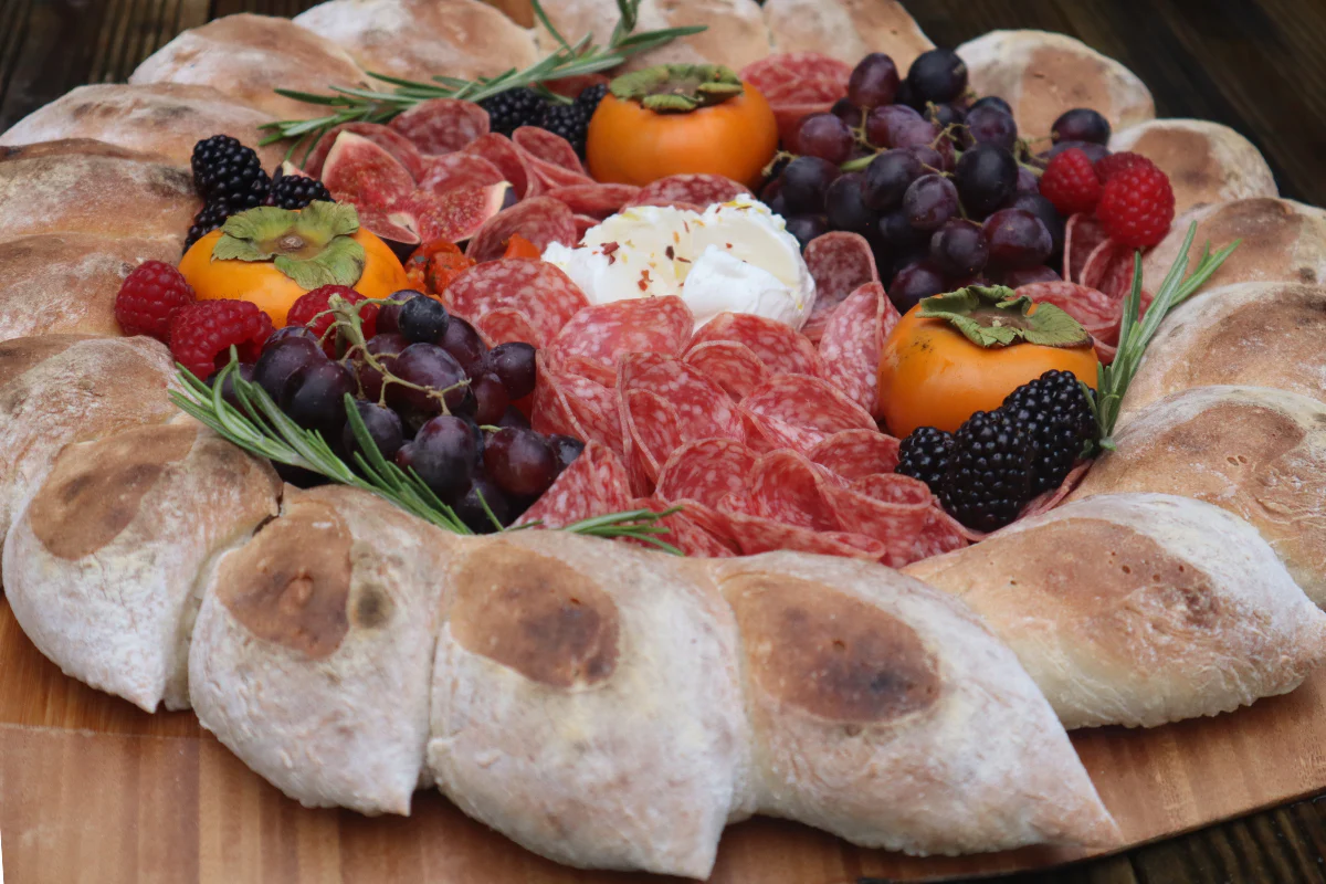 A Christmas wreath made out of bread. Cold meats, fruits and cheese fill the middle.