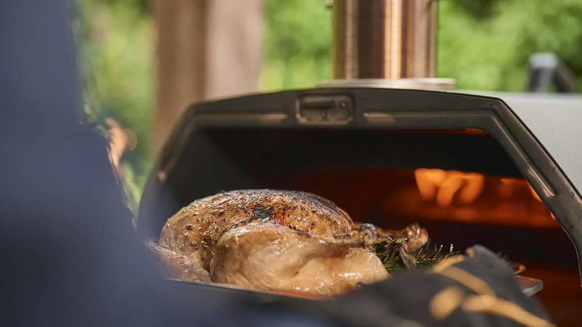 A whole roasted chicken coming out of Ooni Karu 2 Pro