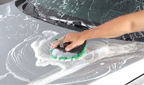 The hood of a silver car being washed by hand.