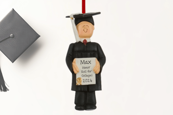 Personalized graduation figurine ornament with cap and gown holding diploma sign, custom name and year.