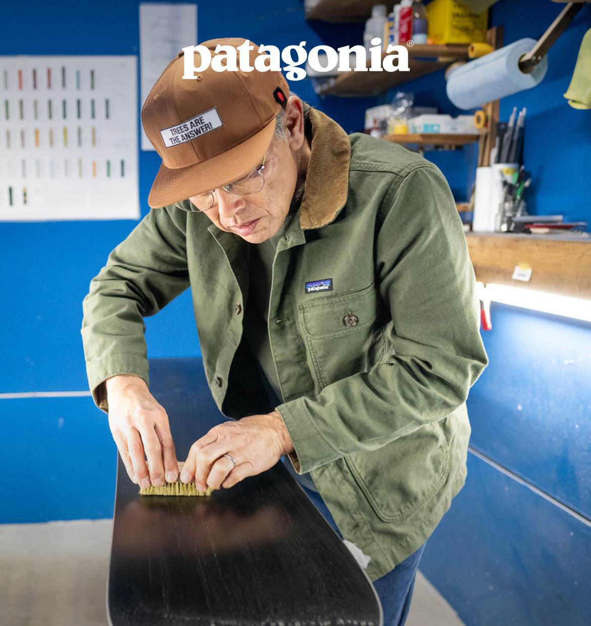 A man runs a wax brush along the base of a snowboard.