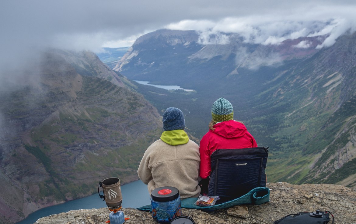 Two hikers sit side by side overlooking a glacial valley.