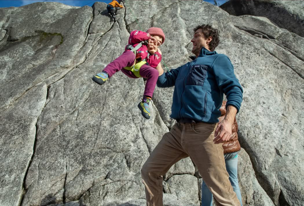 A person holds a baby in front of a rock.