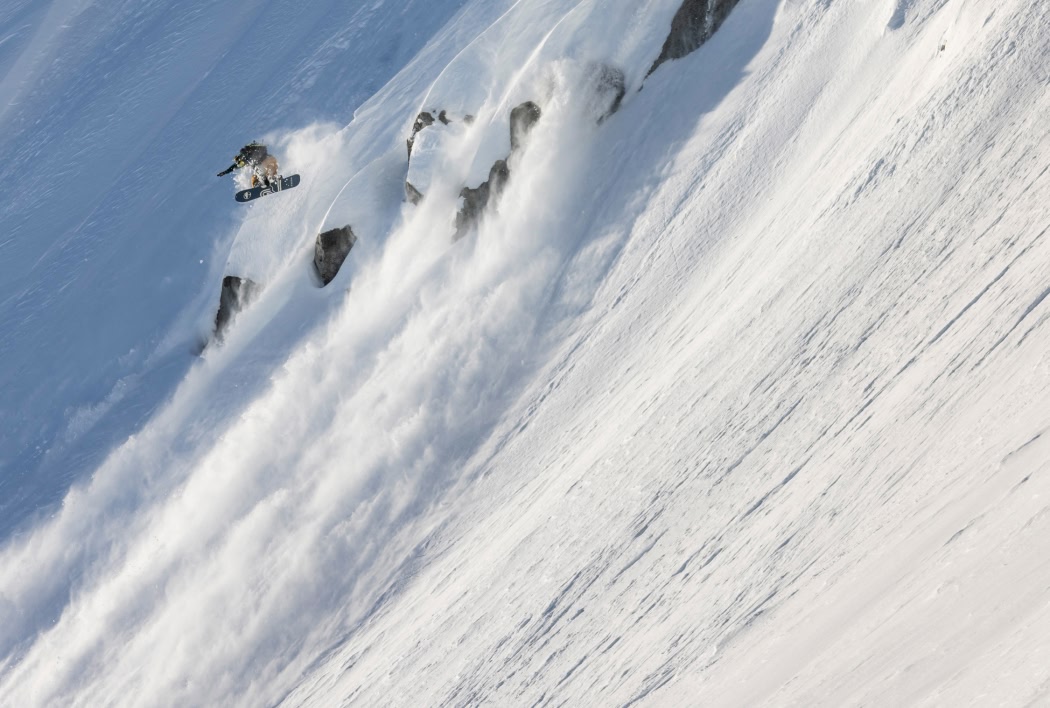 A snowboarder catches air on a steep mountain.