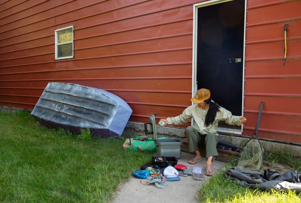 A person sits on a doorstep arranging fishing gear.