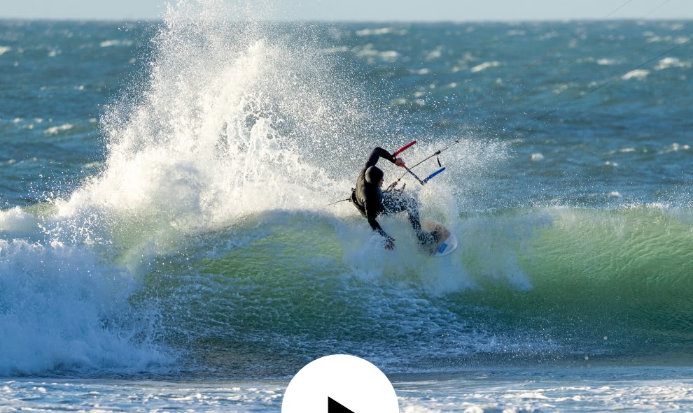 A kite surfer hits the lip of a wave on a windy day.