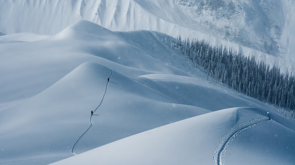 Photo of two backcountry skiers following a skintrack through rolling snow-covered hills.