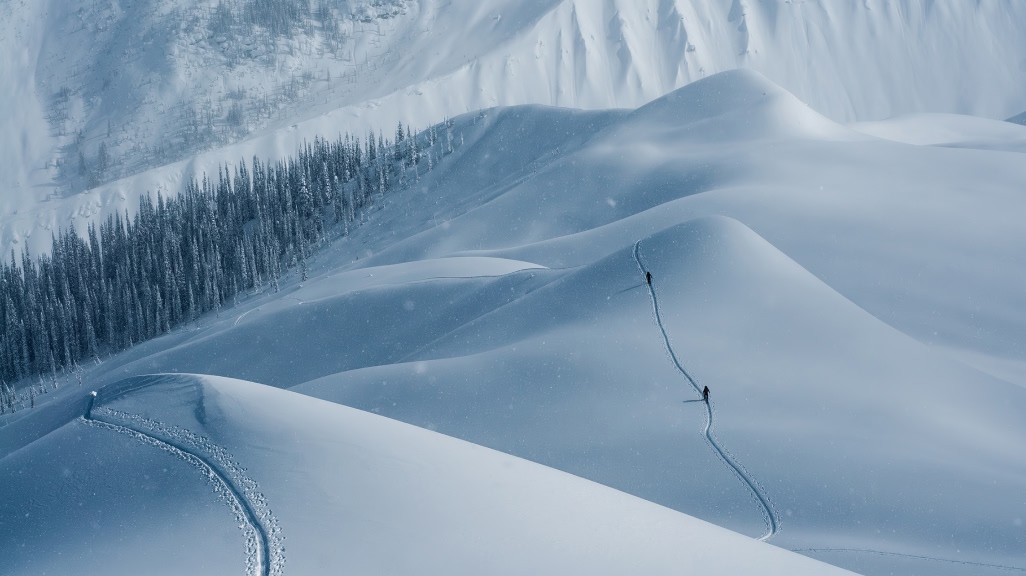  Two people hike across a snowy mountain on skis.