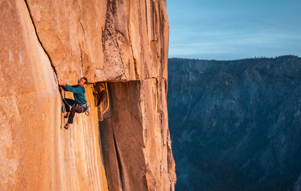A person reaches for a hold while climbing a rock