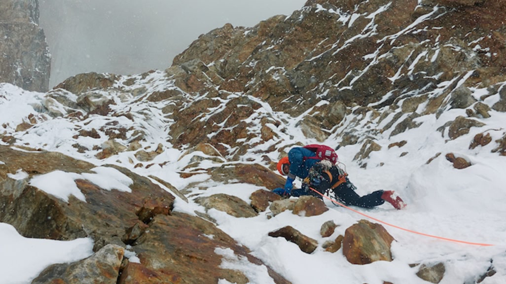 A person climbs up a snowy mountain. 