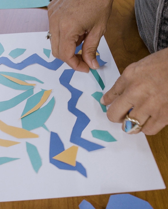 A person places construction paper cutouts on a white piece of paper to make a design.